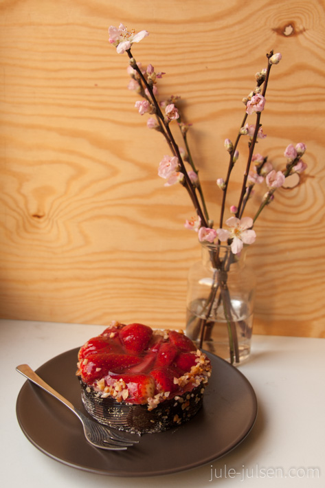 Erdbeertoertchen auf Teller und dahinter Vase mit rosa Bluetenzweigen Erdbeertoertchen auf Teller und dahinter Vase mit rosa Bluetenzweigen