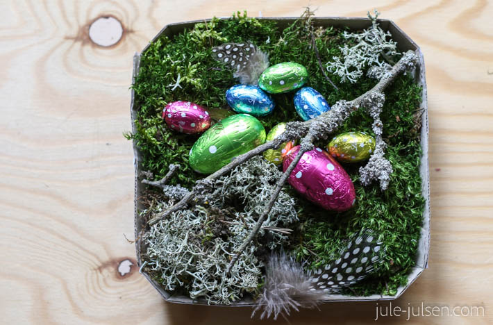 Osterkoerbchen aus Karton mit Moos, Flechte, Zweigen und bunten Schokoeiern Osterkoerbchen aus Karton mit Moos, Flechte, Zweigen und bunten Schokoeiern