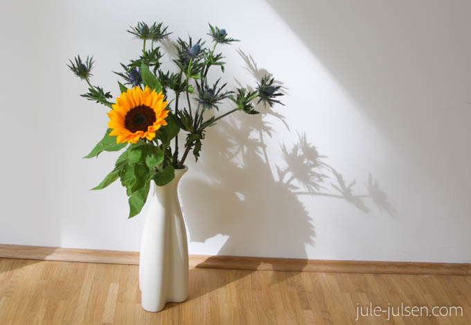 Blumenstrauss mit Disteln und einer Sonnenblume in schlichter weißer Vase Blumenstrauss mit Disteln und einer Sonnenblume in schlichter weißer Vase